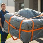 Traslocatori professionisti trasportano un divano imballato fuori da una casa. Immagine che rappresenta l'affidabilità di una ditta di trasloco.